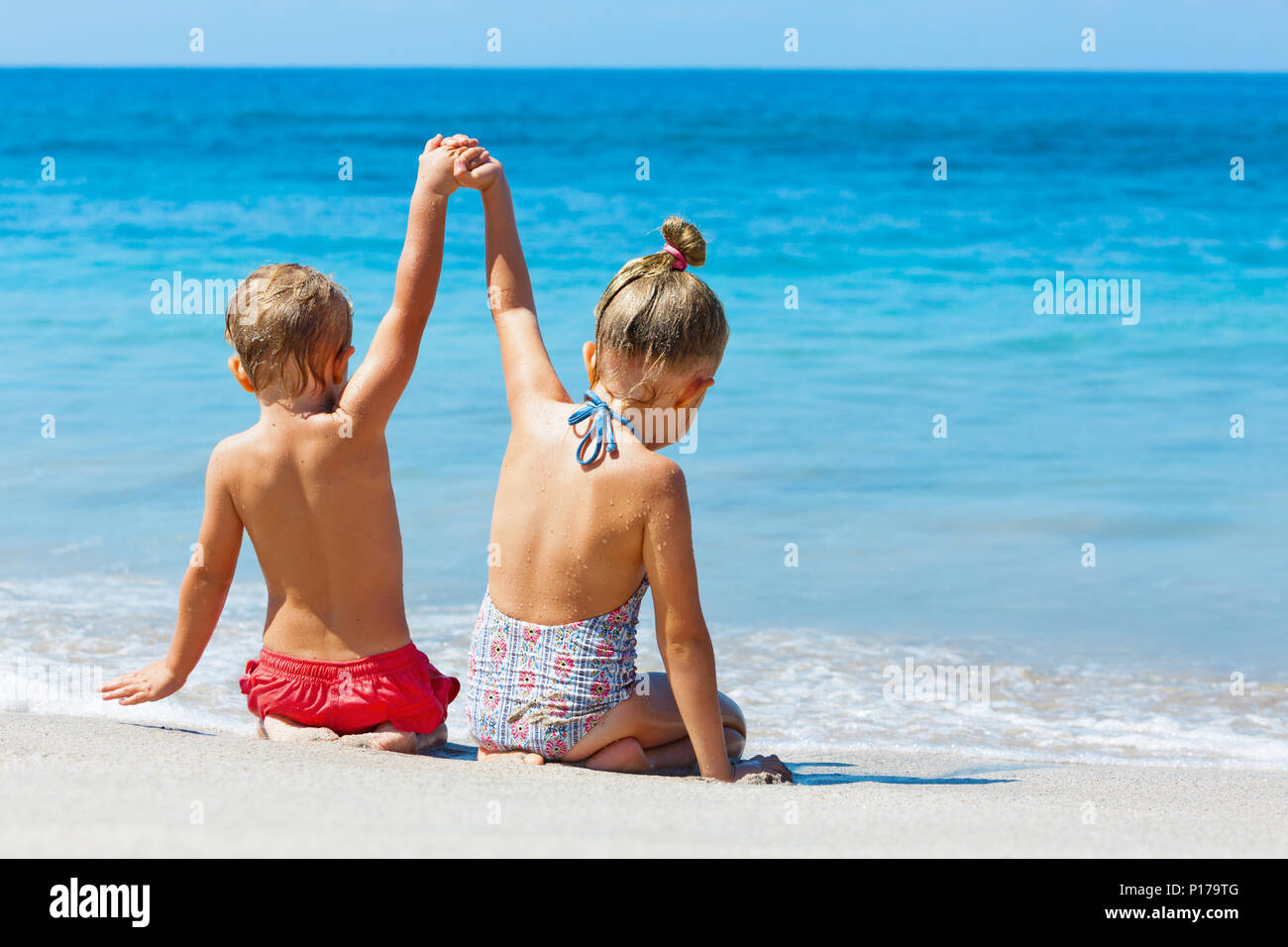 Happy kids have fun in sea surf on sand beach.  Children sit in water pool with hands up. Travel lifestyle, swimming activities in family holiday Stock Photo