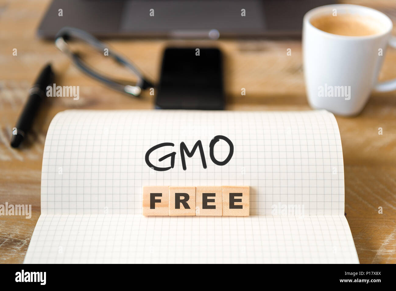Closeup on notebook over vintage desk surface, front focus on wooden blocks with letters making GMO Free text. Stock Photo