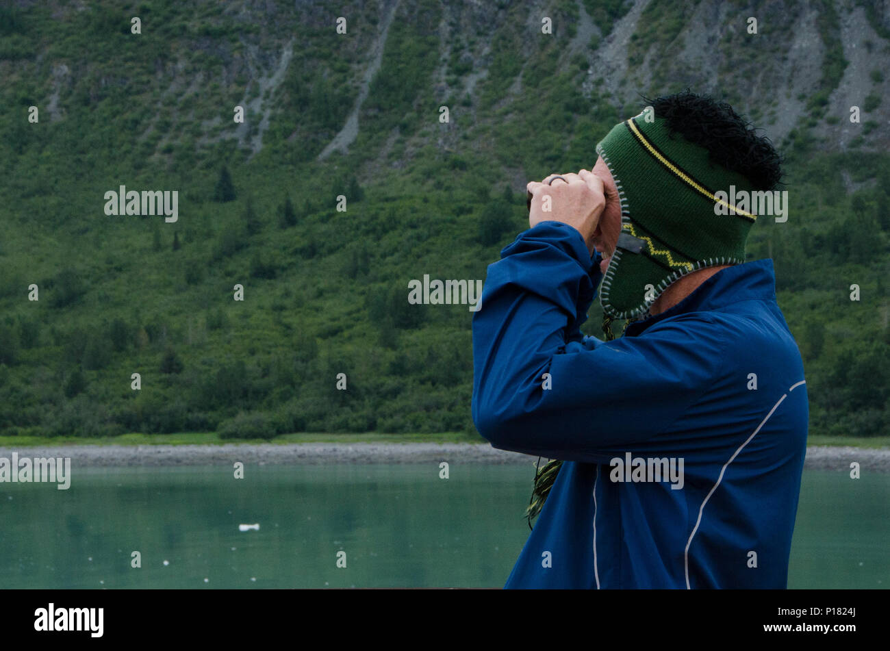 Men with binoculars looking out with coastal background.  Man looking for wildlife with binoculars, cold weather. Coastal Alaska from cruise ship. Stock Photo
