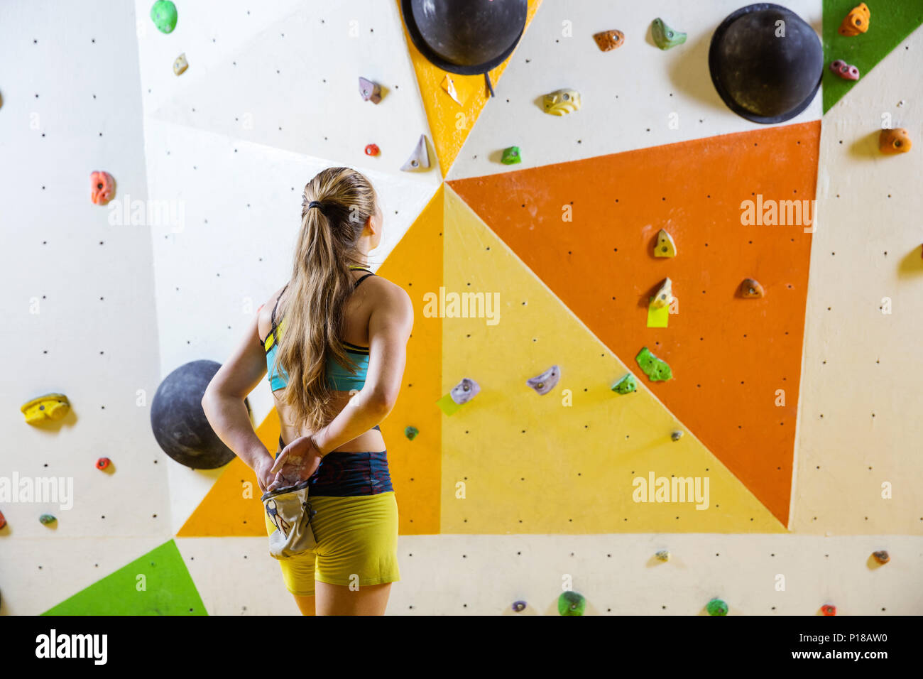 Young woman putting chalk on hands and looking at bouldering problem she is going to climb. In indoor climbing gym. Stock Photo