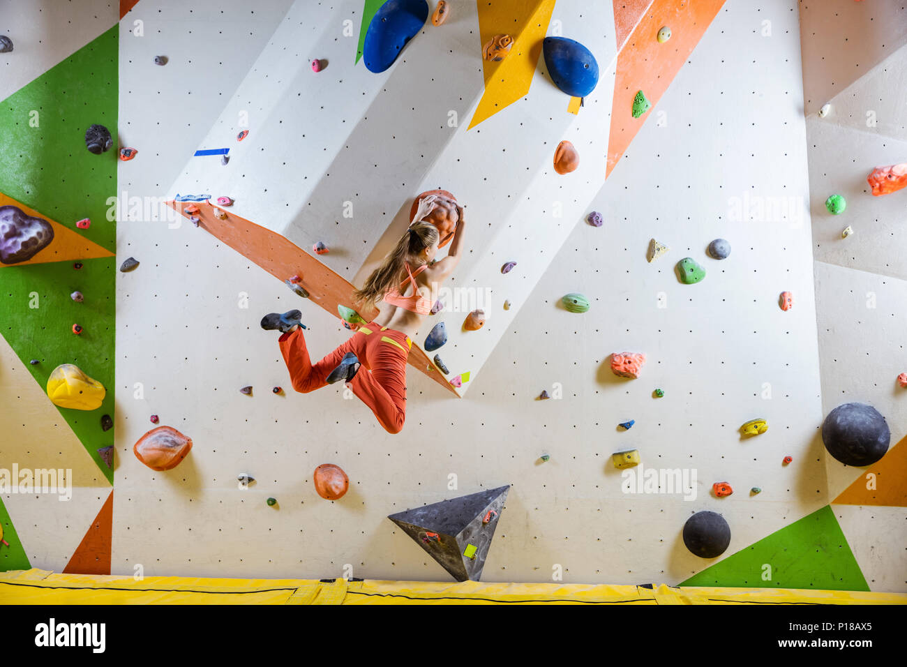 Young athletic woman jumping on climbing hold in indoor bouldering gym