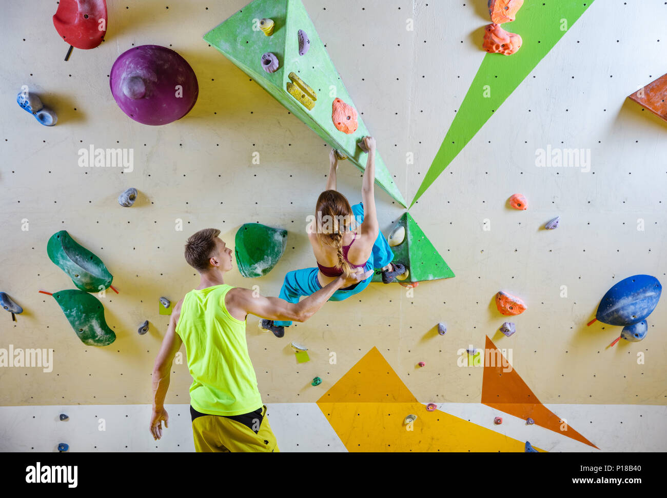 Rock climbers in climbing gym. Young woman climbing bouldering problem (route), male instructor