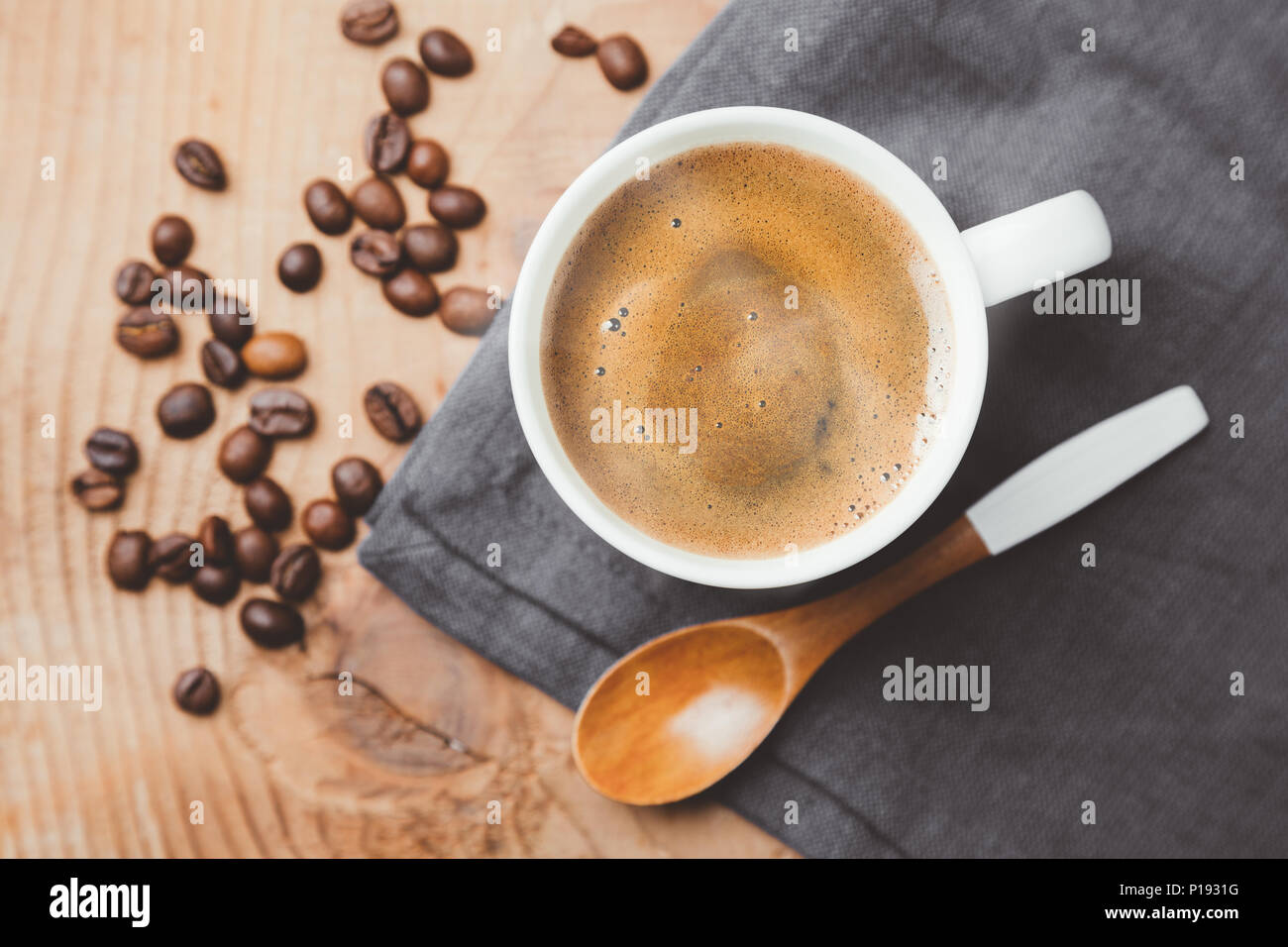 Cup of steaming coffee cup with a wooden spoon and roasted coffee beans on gray textile . Top view, flat lay Stock Photo