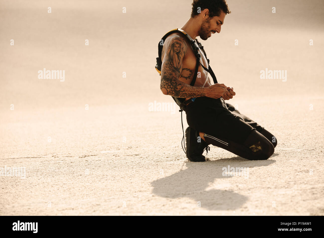 Young man taking a rest after workout on desert sand. Fit man relaxing after intense training outdoors. Stock Photo