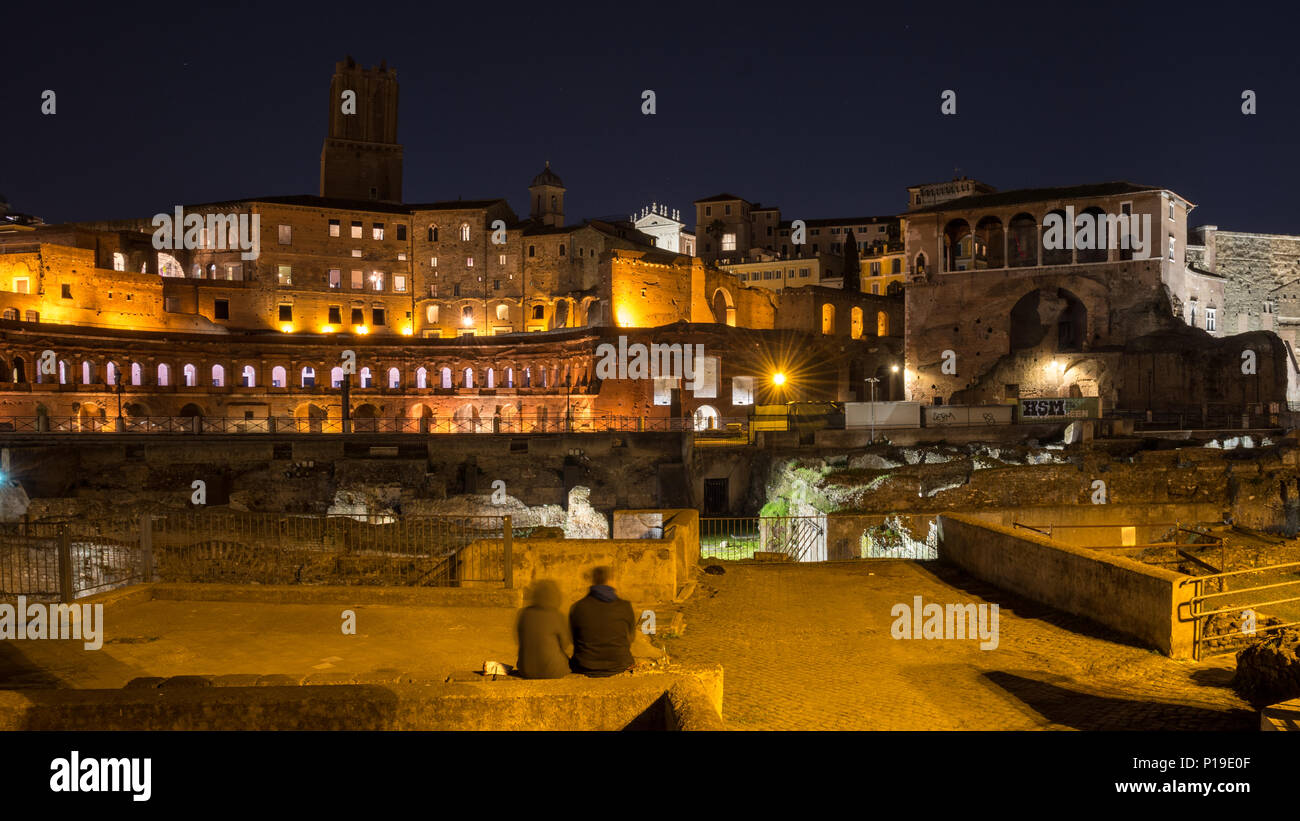 Rome, Italy - March 25, 2018: A couple sit amongst the ruins of Trajan's Forum and Market in Rome at night. Stock Photo
