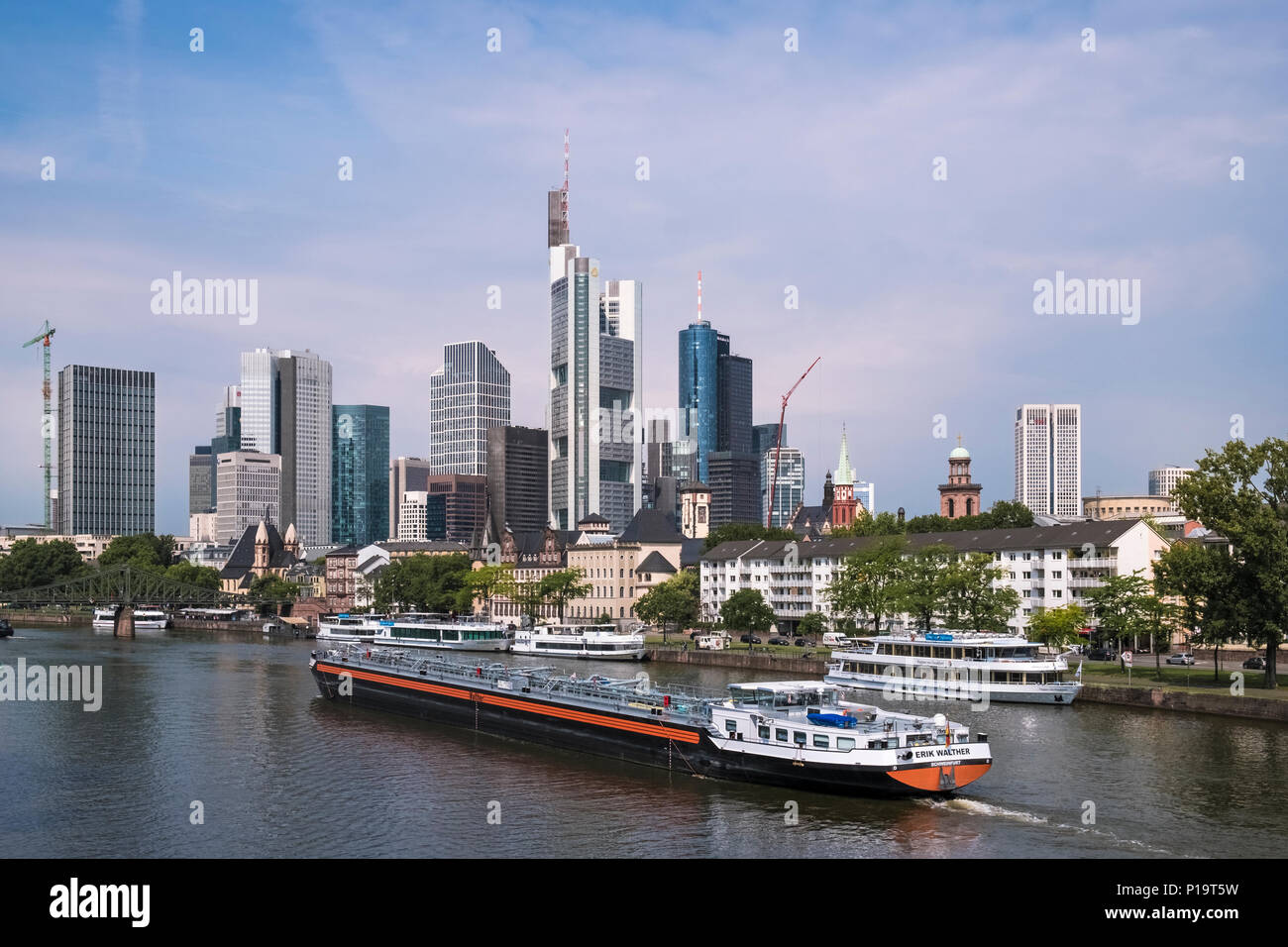 A large barge travels on the river Main, past the citys modern architecture skyscraper skyline, Frankfurt am Main, Hesse, Germany Stock Photo