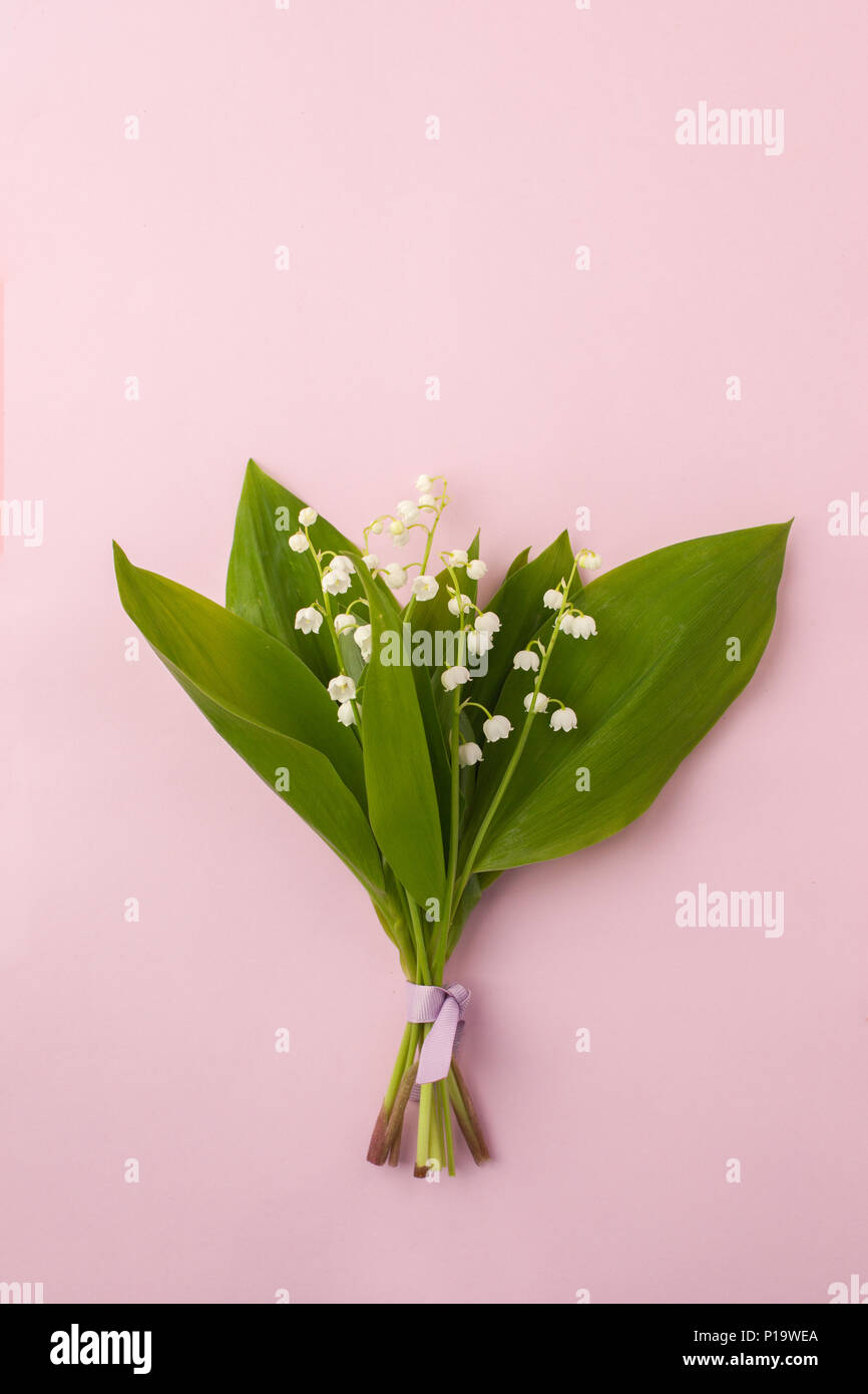 Festive flower lily of the valley composition on the pastel pink background. Overhead view, may-lily bouquet with copy space Stock Photo