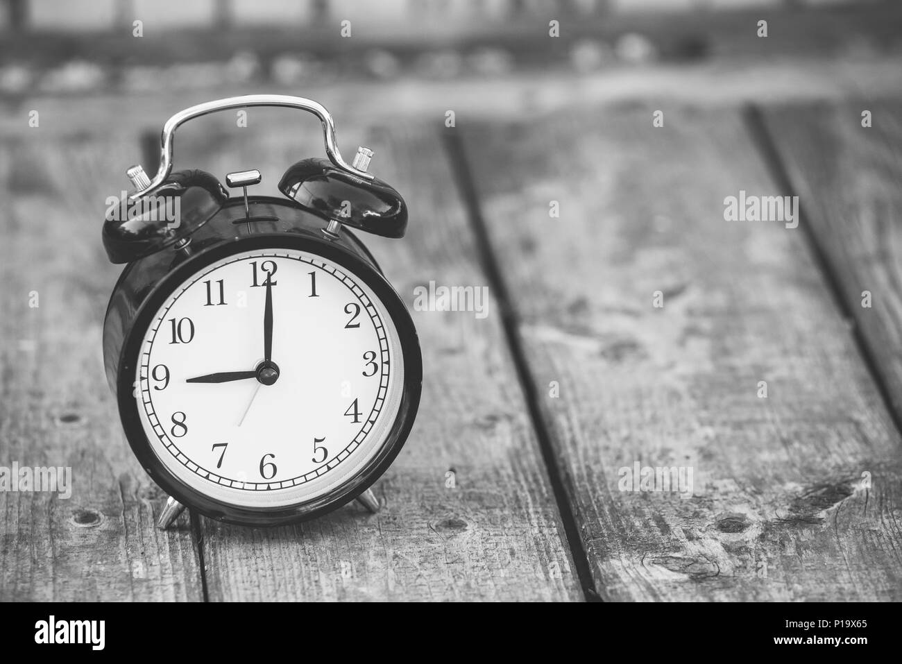 alarm clock showing five o'clock on wooden background, black and white