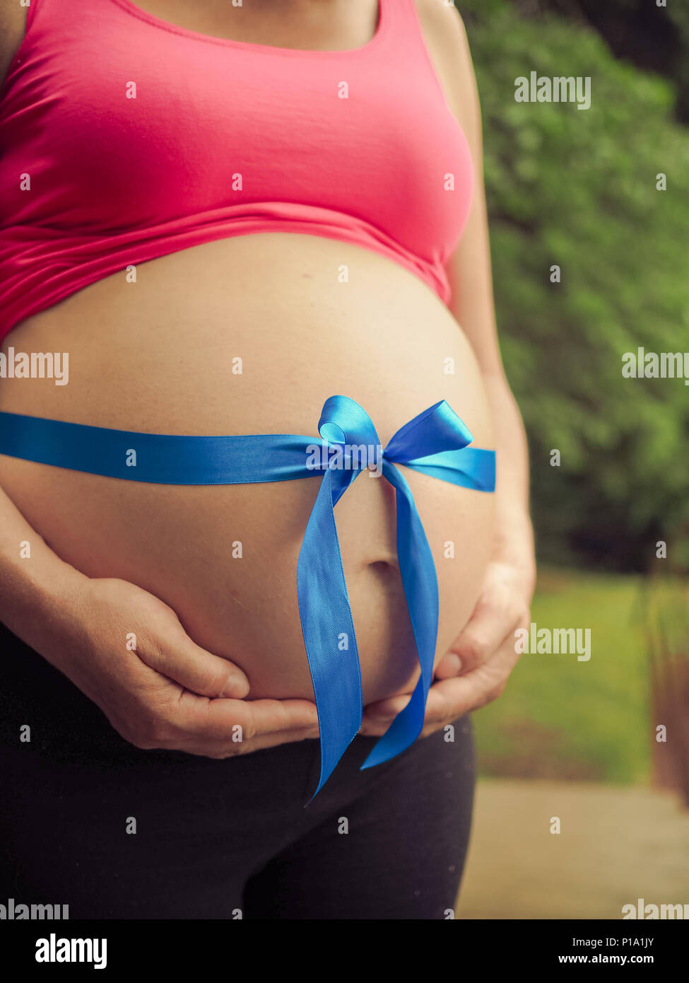 Big pregnant belly with blue ribbon, photographed outdoors in the nature Stock Photo