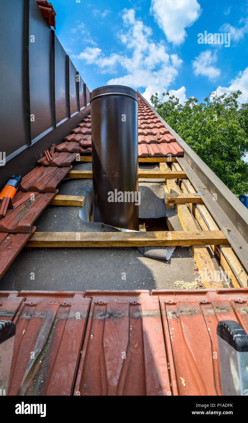 Installing external chimney trough a house roof with roof tiles. Uncovering  roof and constructing an aluminium round chimney in a family private house  Stock Photo - Alamy