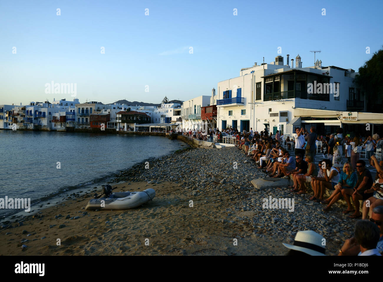 Tourists sitting along beach waiting for sunset at Mykonos, Cyclades islands, Greece Stock Photo