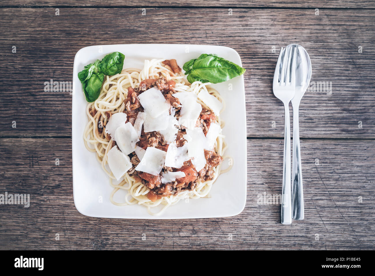 directly above shot of pasta with Bolognese sauce, basil and grated Parmesan cheese on rustic wooden table Stock Photo