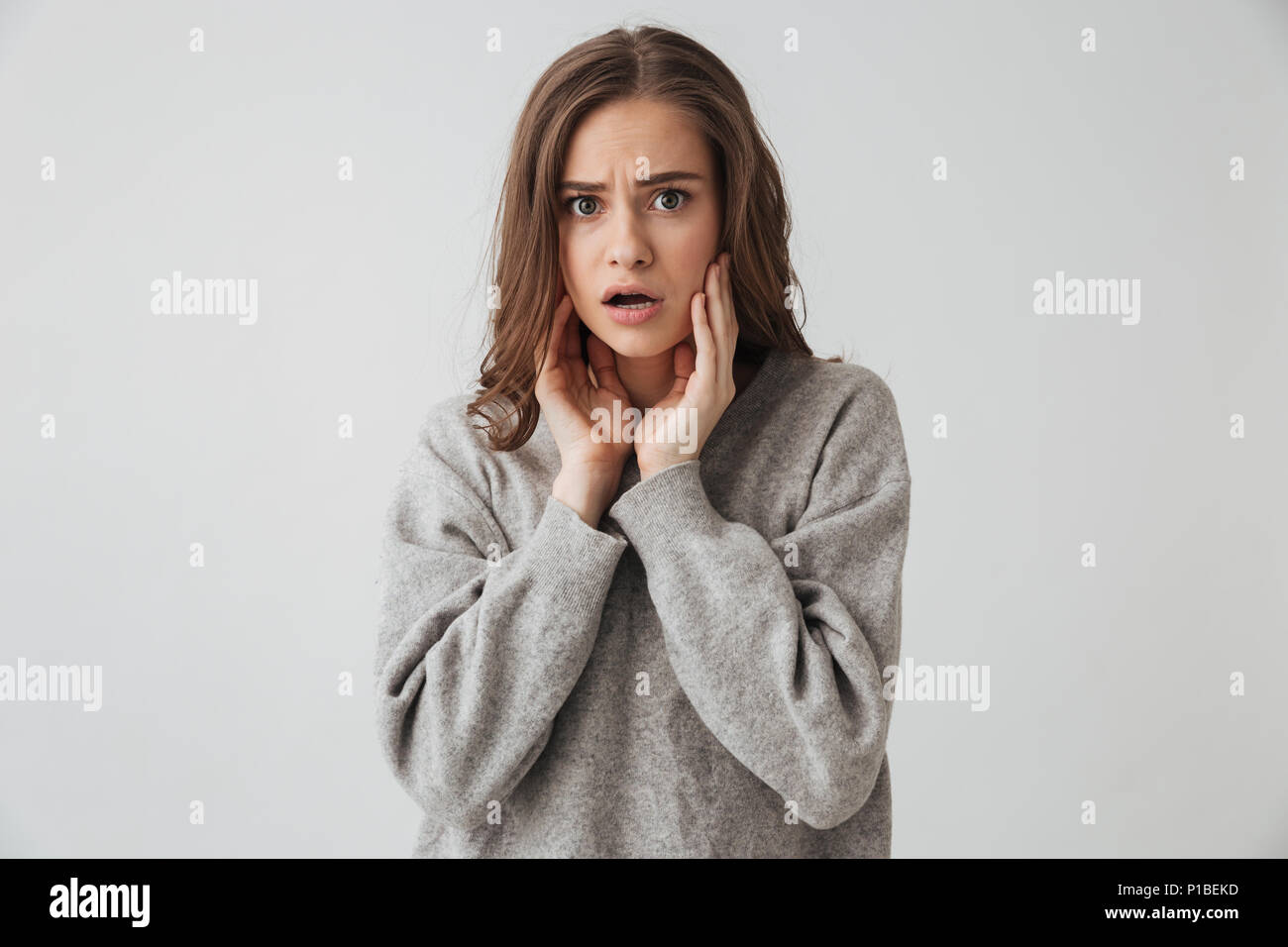 Shocked woman in sweater touching her cheeks and looking at