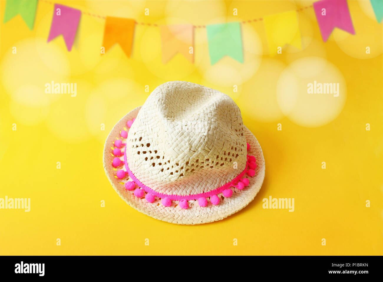 Festa Junina, Brazilian June party greeting card, invitation with straw hat and blurred yellow background with bunting flags decoration and bokeh lights. Festive design. Stock Photo