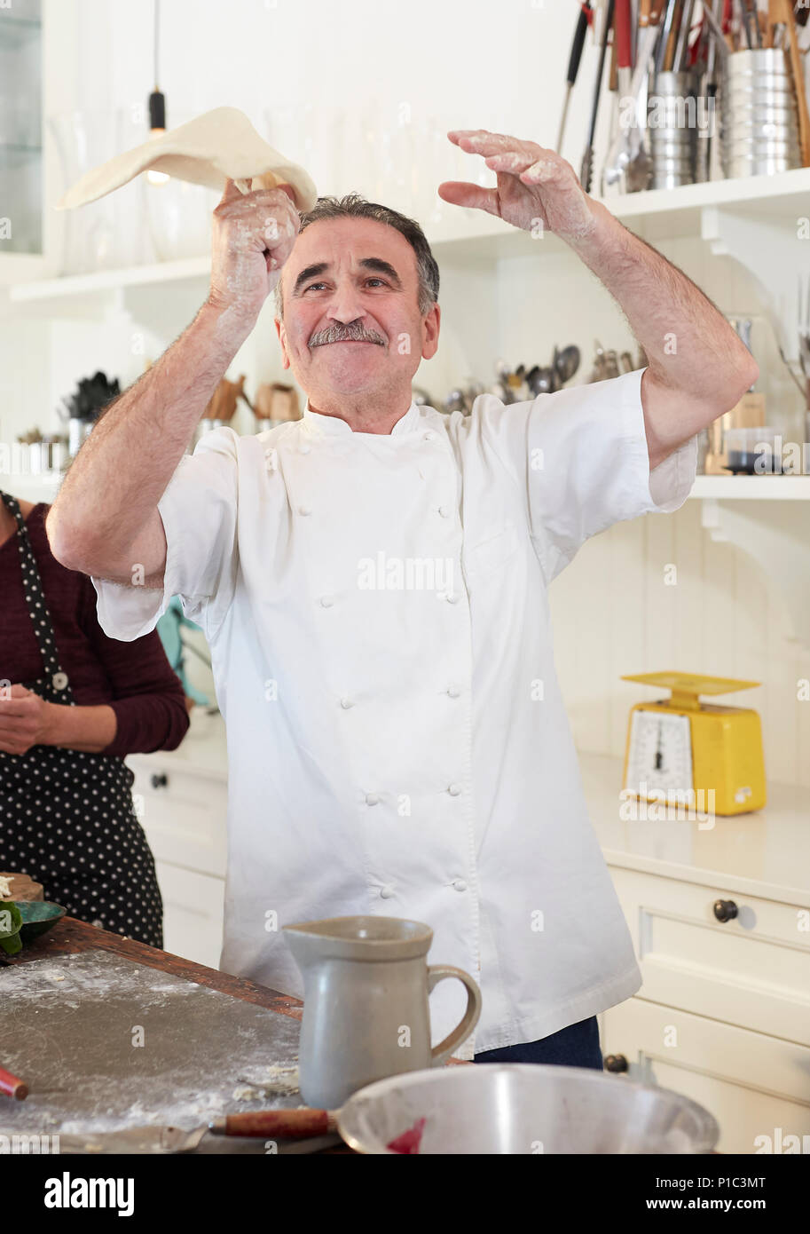 Playful senior chef tossing pizza dough in kitchen Stock Photo