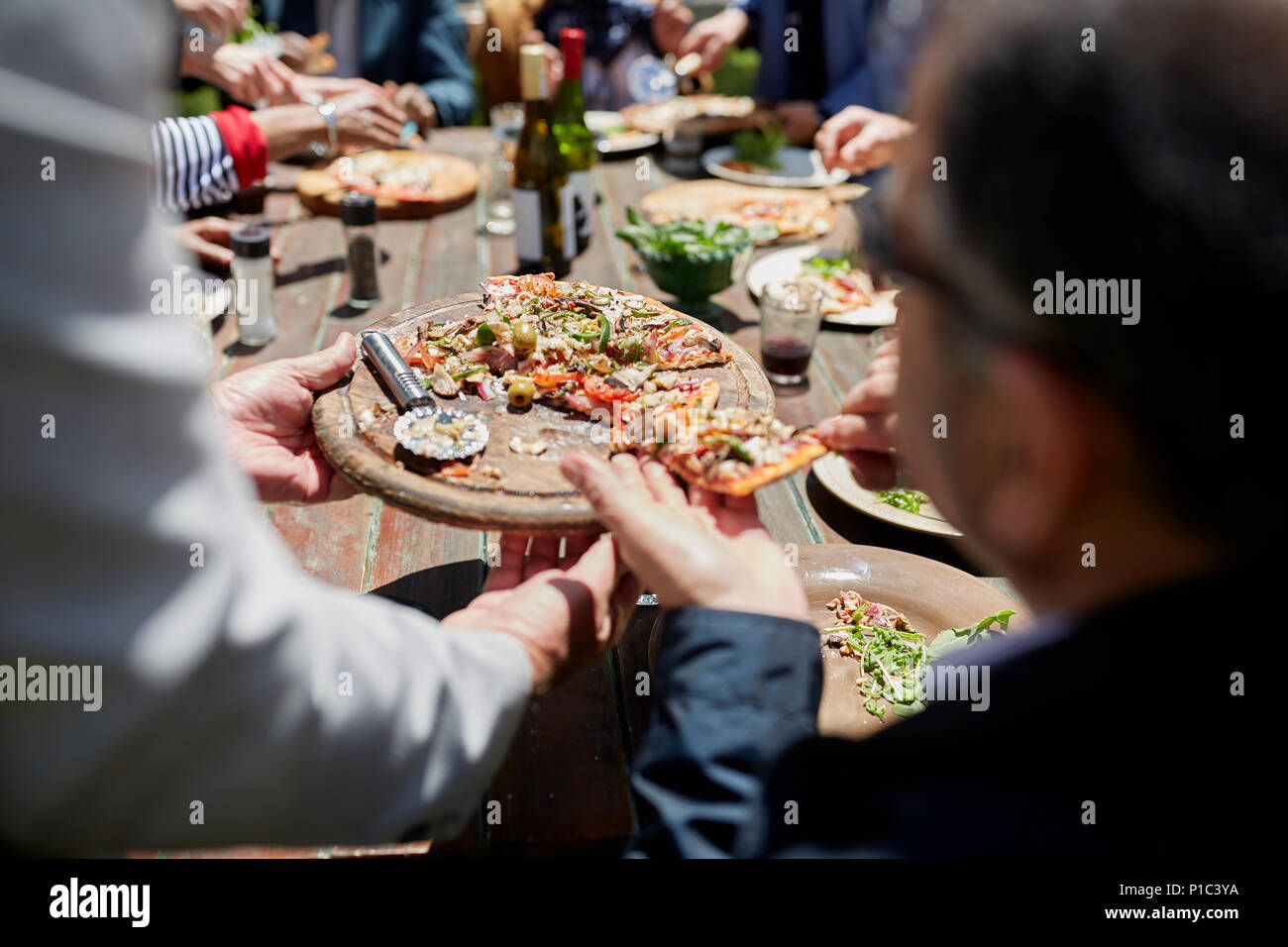 Friends sharing homemade pizza at sunny patio table Stock Photo