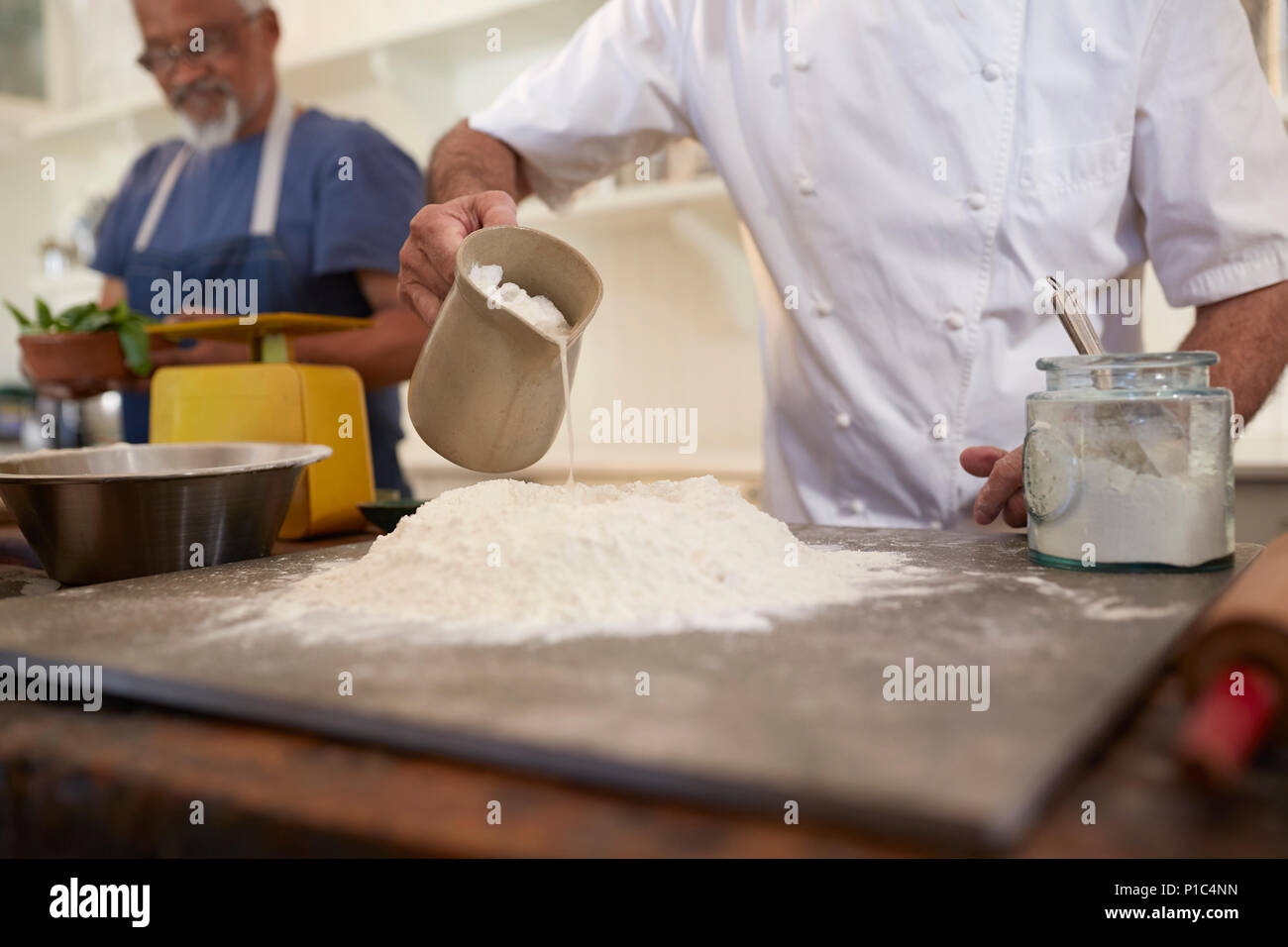 Close up chef pouring water into pizza dough flour nest in cooking class Stock Photo