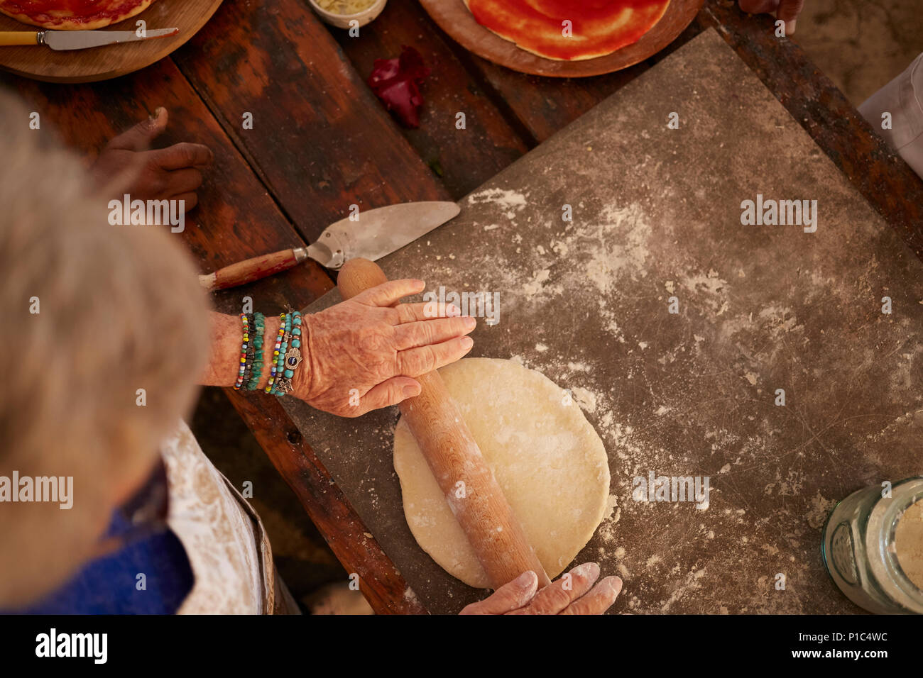 Overhead view senior woman rolling, making fresh pizza dough Stock Photo