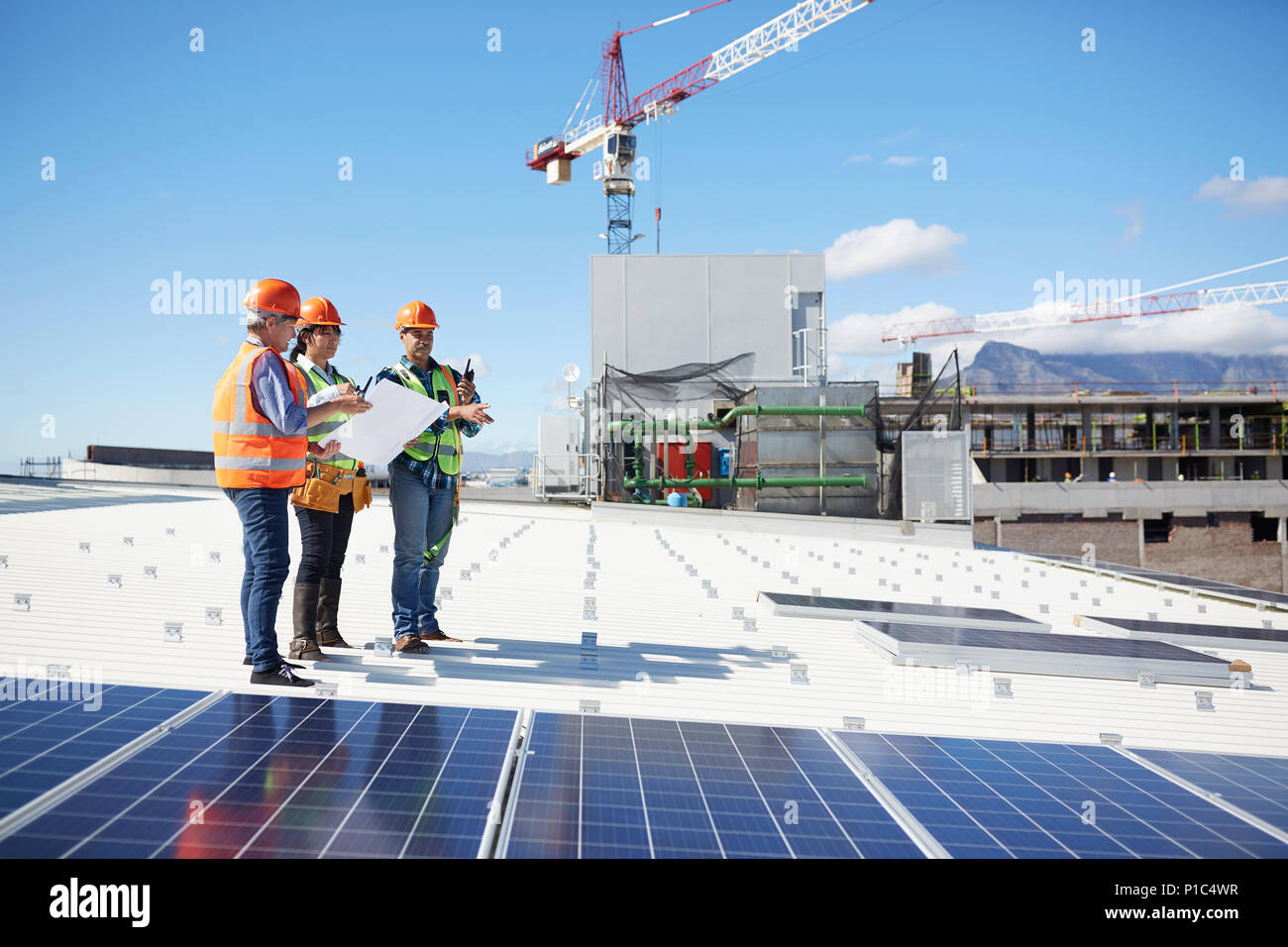 Engineers with blueprint at solar panels at sunny power plant Stock Photo