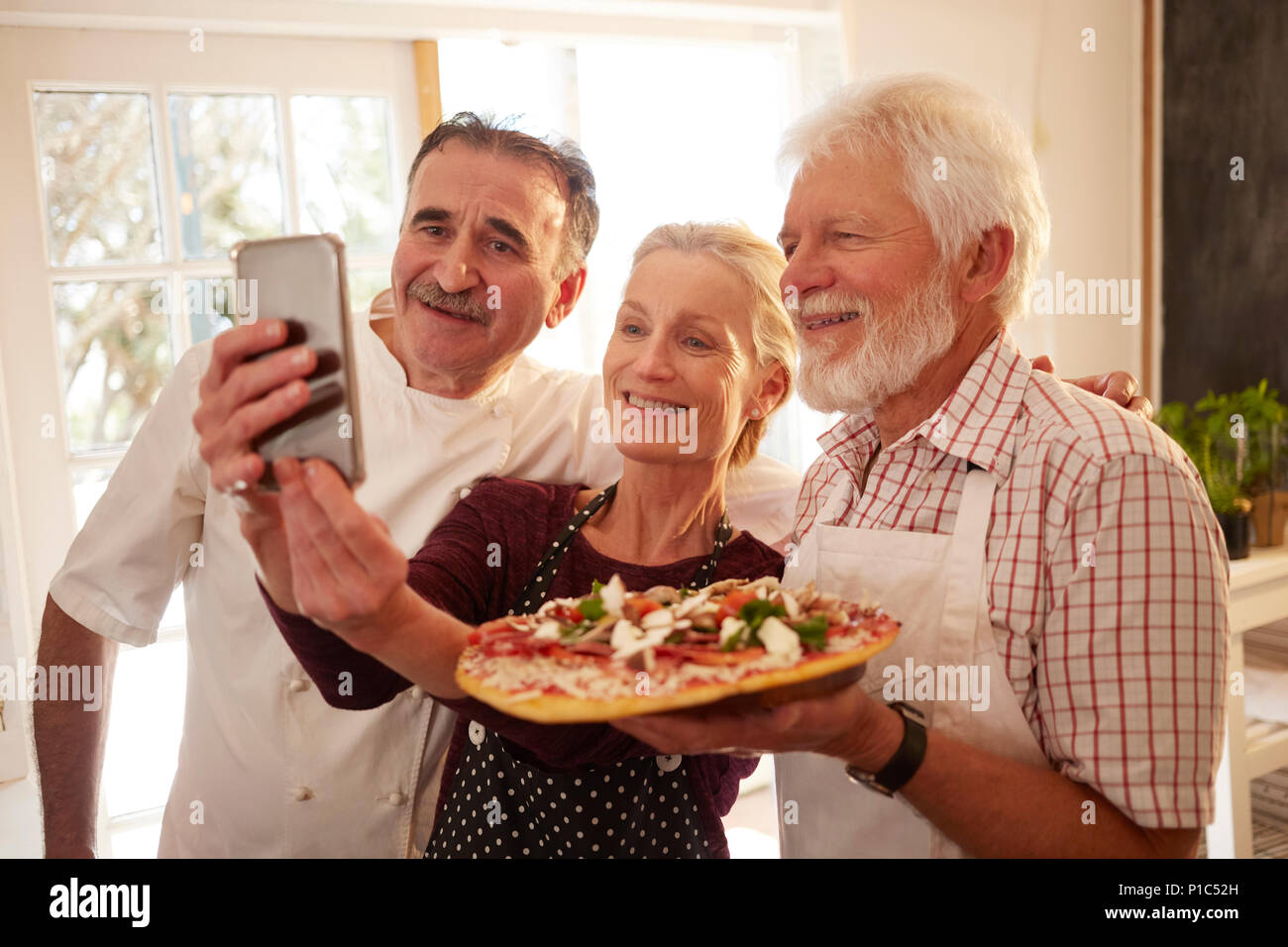 Chef and senior couple taking selfie with pizza in cooking class Stock Photo