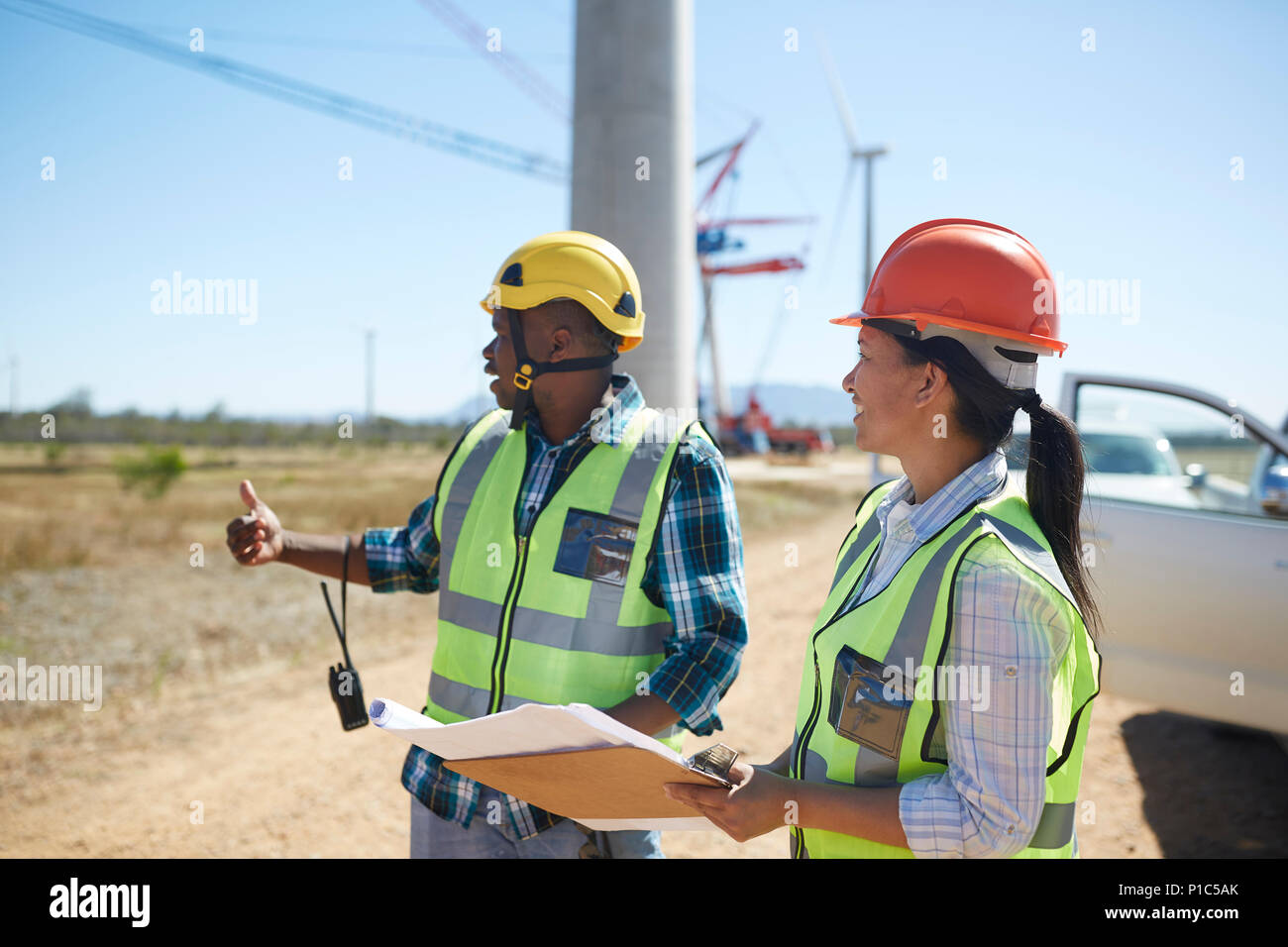 Engineers with blueprints talking at sunny power plant Stock Photo