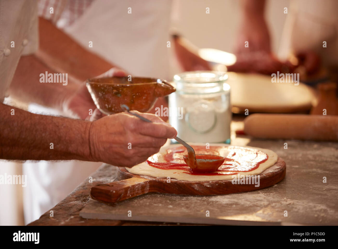 Close up man spreading marinara sauce on dough in pizza cooking class Stock Photo