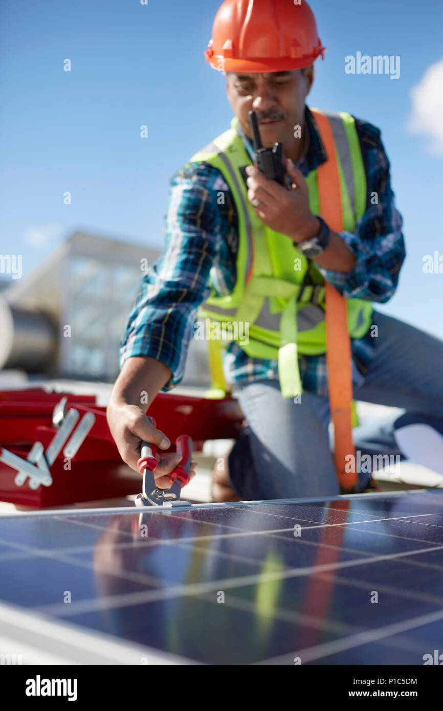 Male engineer with walkie-talkie repairing solar panel at power plant Stock Photo