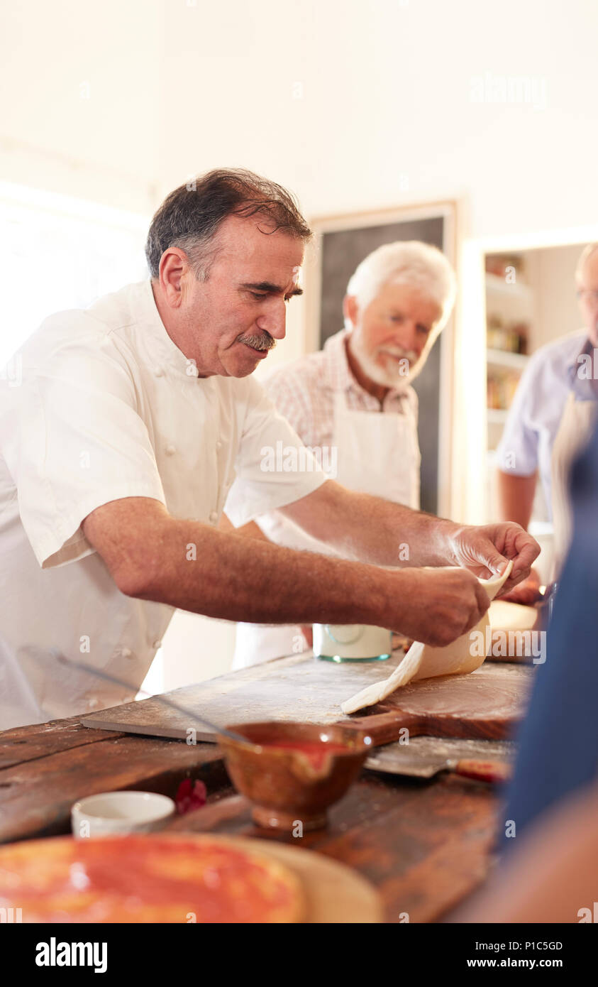 Focused chef spreading pizza dough in cooking class Stock Photo