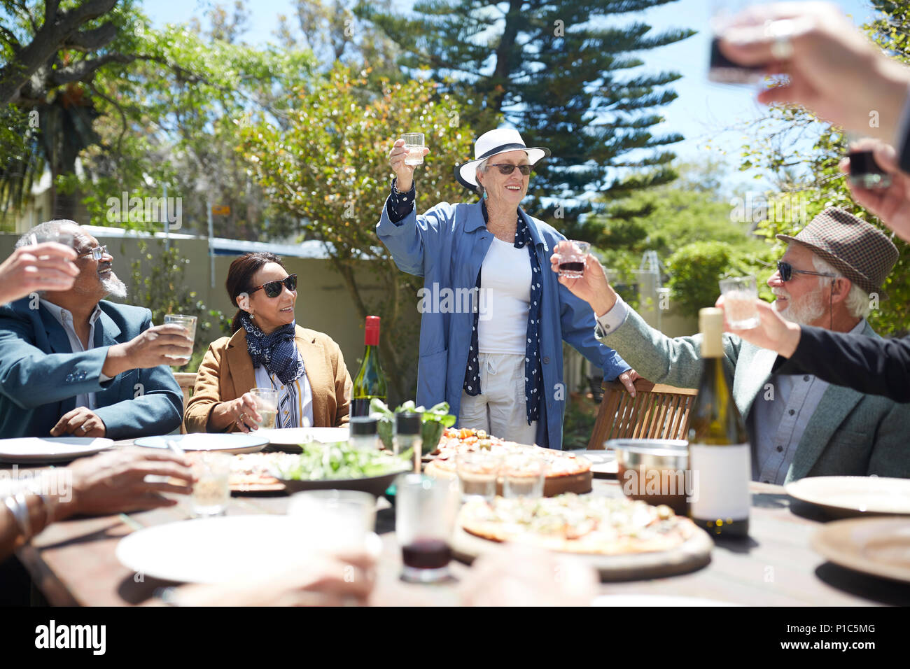 Happy senior woman toasting wine with friends at sunny garden party Stock Photo