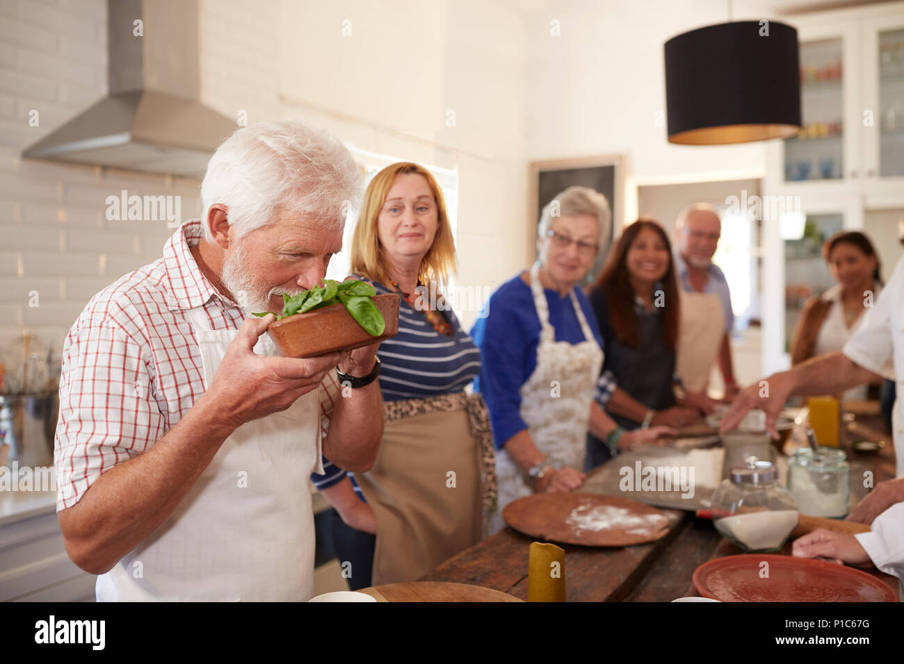Active senior friends taking cooking class, smelling fresh basil Stock Photo