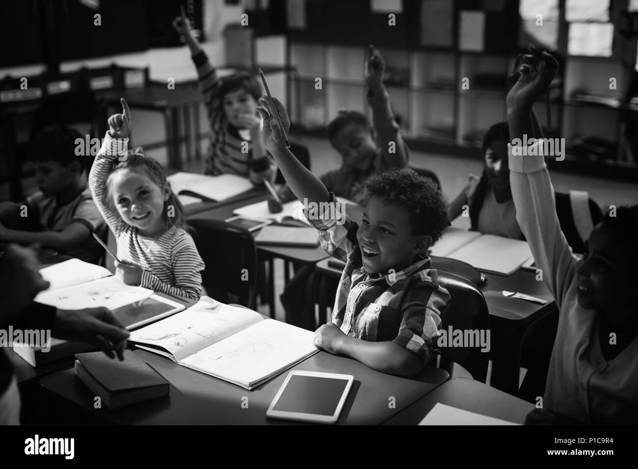 Schoolkids raising their hands in classroom Stock Photo