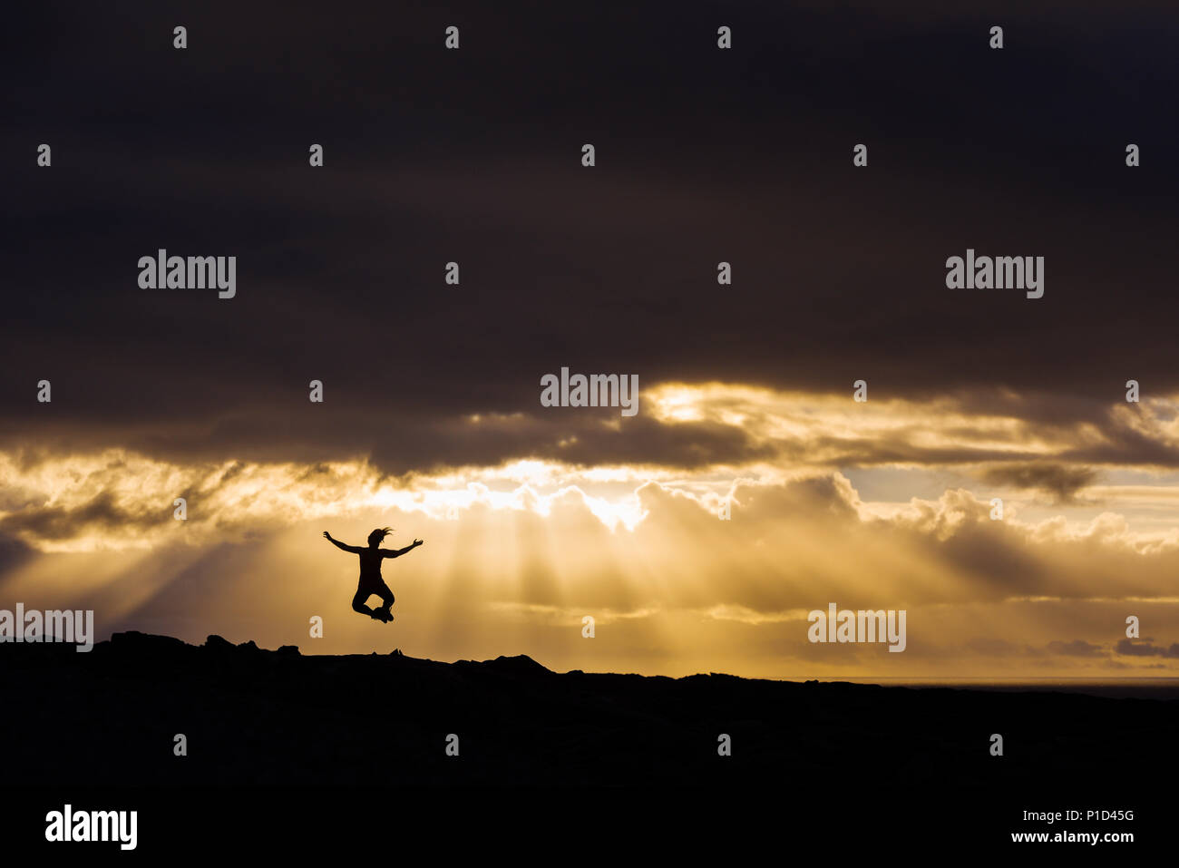 Woman jumping in the air and clicking heels together during dramatic sunset Stock Photo