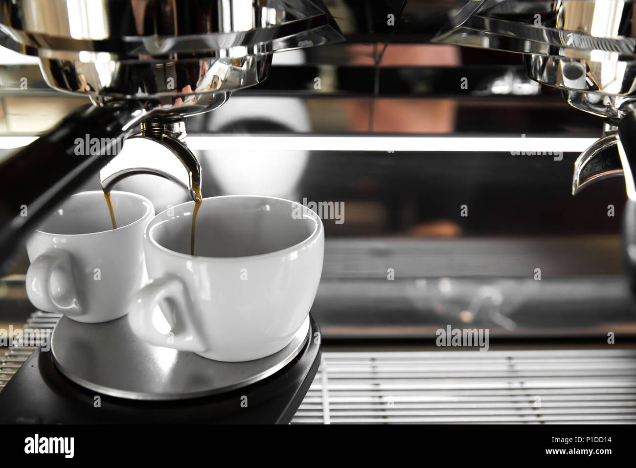 Italian espresso machine on a counter in a restaurant dispensing freshly brewed coffee into two small cups Stock Photo