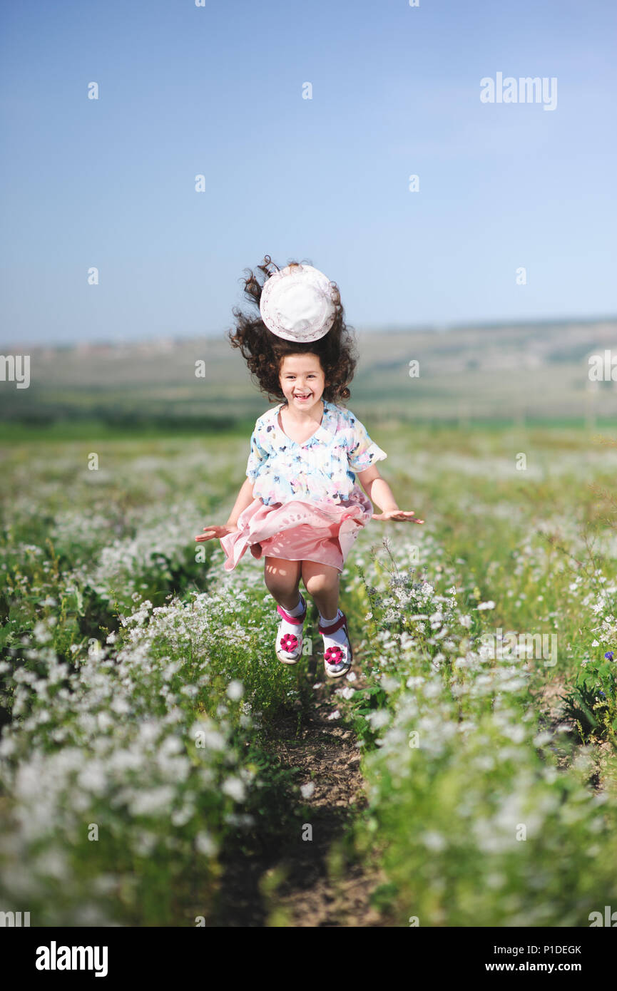pretty happy little girl jumping with hat flying off her head in summer