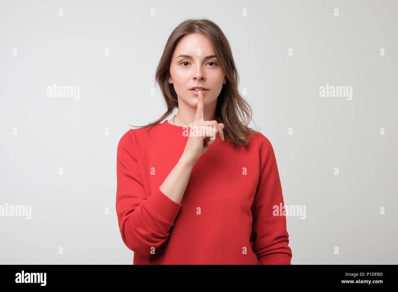 Beautiful european woman in red pulover showing silence sign Stock Photo