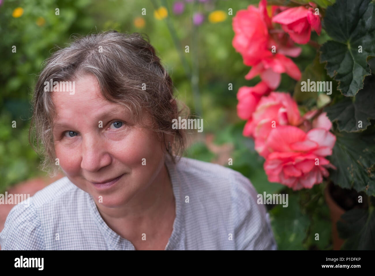 Mature caucasian woman sitting in her garden near flowers Stock Photo