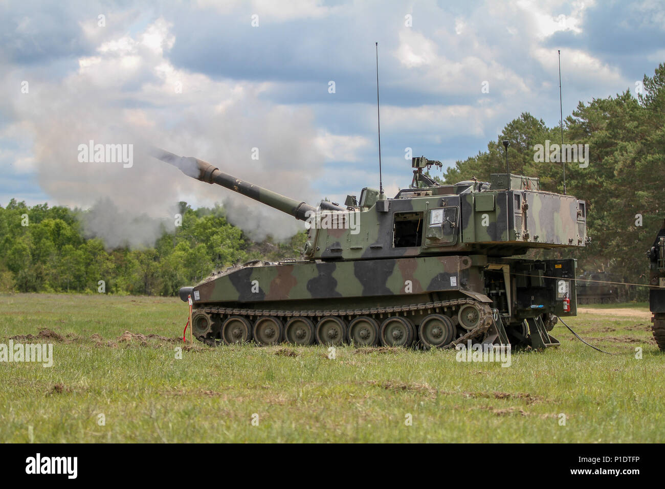 CAMP GRAYLING, Mich. – A M1908 Paladin from the 2-150 Field Artillery Regiment fires the first round of the day during a live fire exercise at Camp Grayling, Mich. June 7, 2018. As a safety precaution, pulling a 25-foot lanyard to ensure the safety of the crew fires the first round from the howitzer. Stock Photo