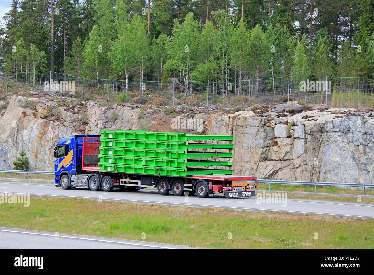 Oversize load transport of industrial objects by blue semi trailer on freeway, side and rear view, on day of summer in Paimio, Finland - June 8, 2018. Stock Photo