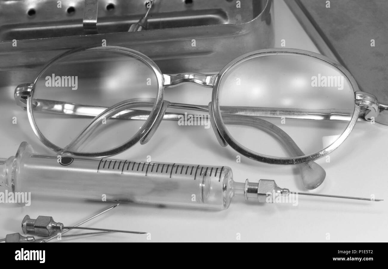 Old syringe in fragile glass with steel needle and the old glasses of the doctor with black and white effect Stock Photo