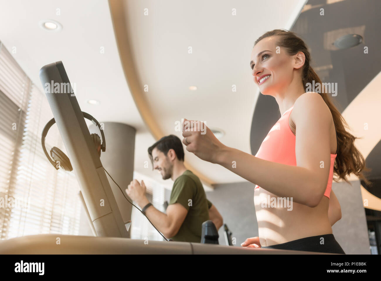 Young woman listening to music while running on a modern treadmill