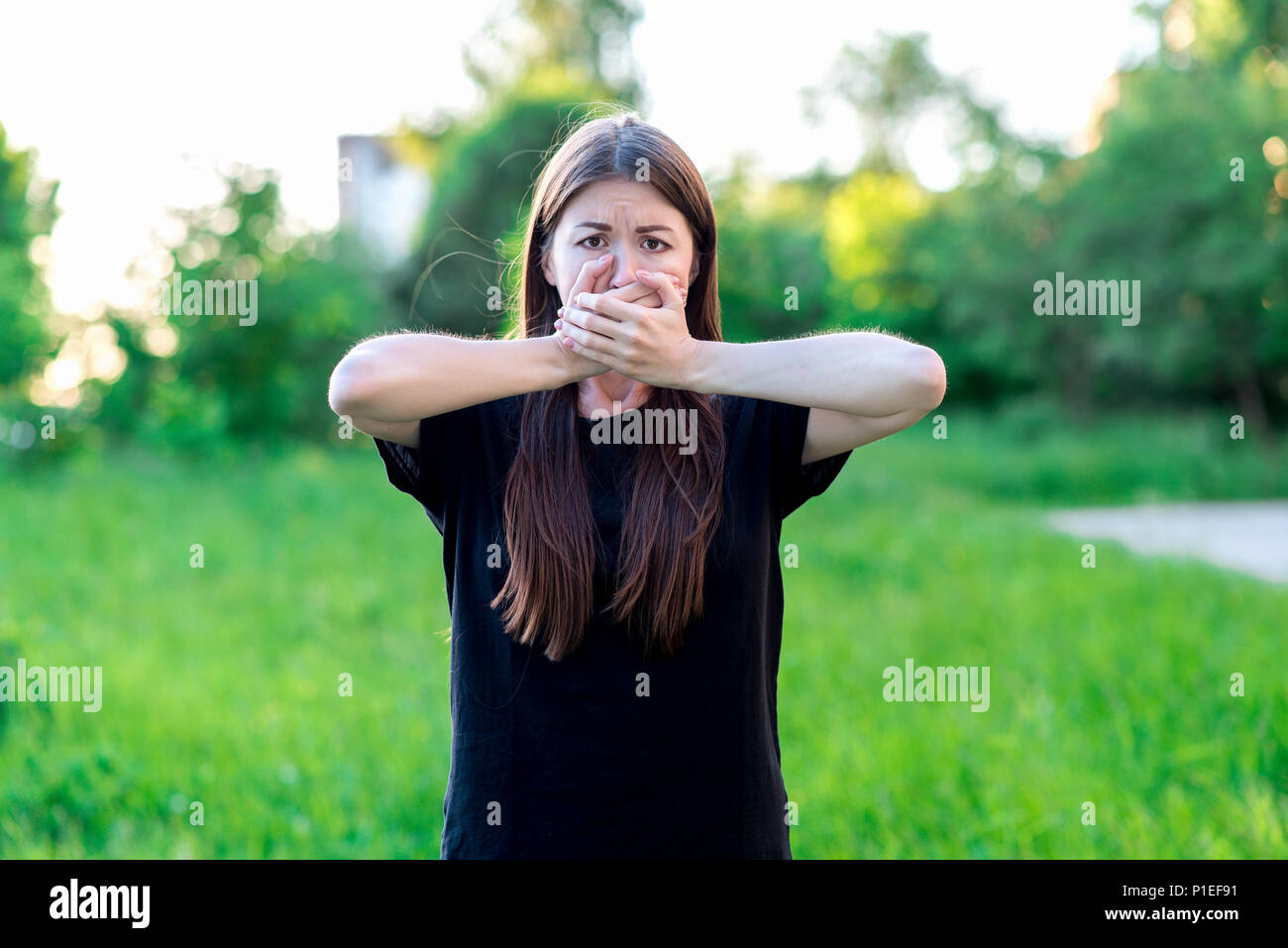 Girl in the summer in park. He covers his mouth with two hands