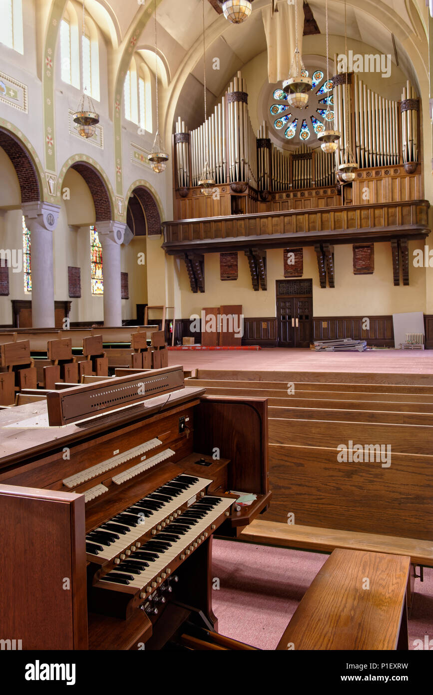 Abandoned church interior showing large pipe organ with two tier keyboard and oak pews, rough and unused. Stock Photo