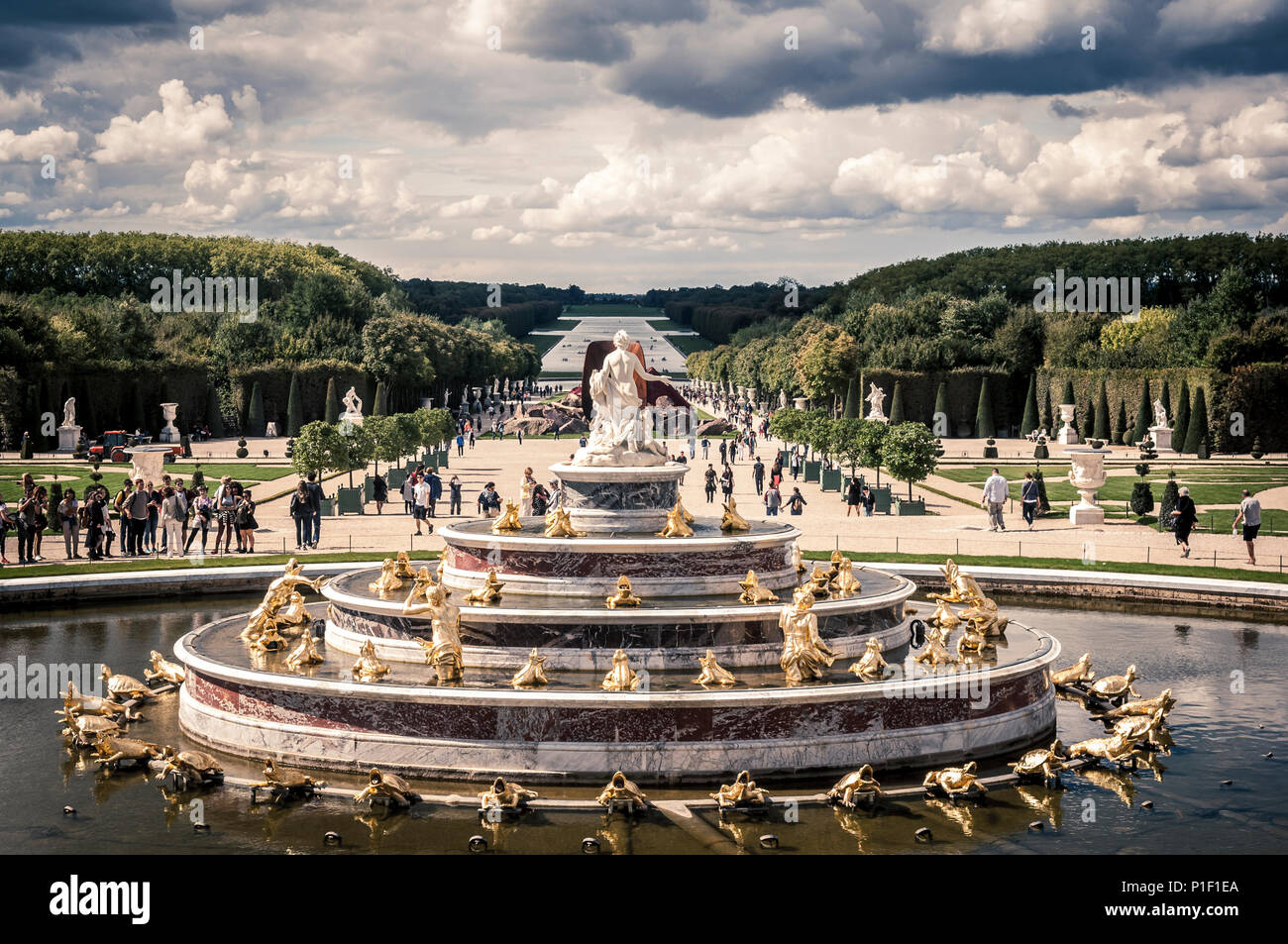 Latona's fountain, in the gardens of Chateau de Versailles, trees in the background against a dramatic blue cloudy sky. Desatured, retro syle. Stock Photo
