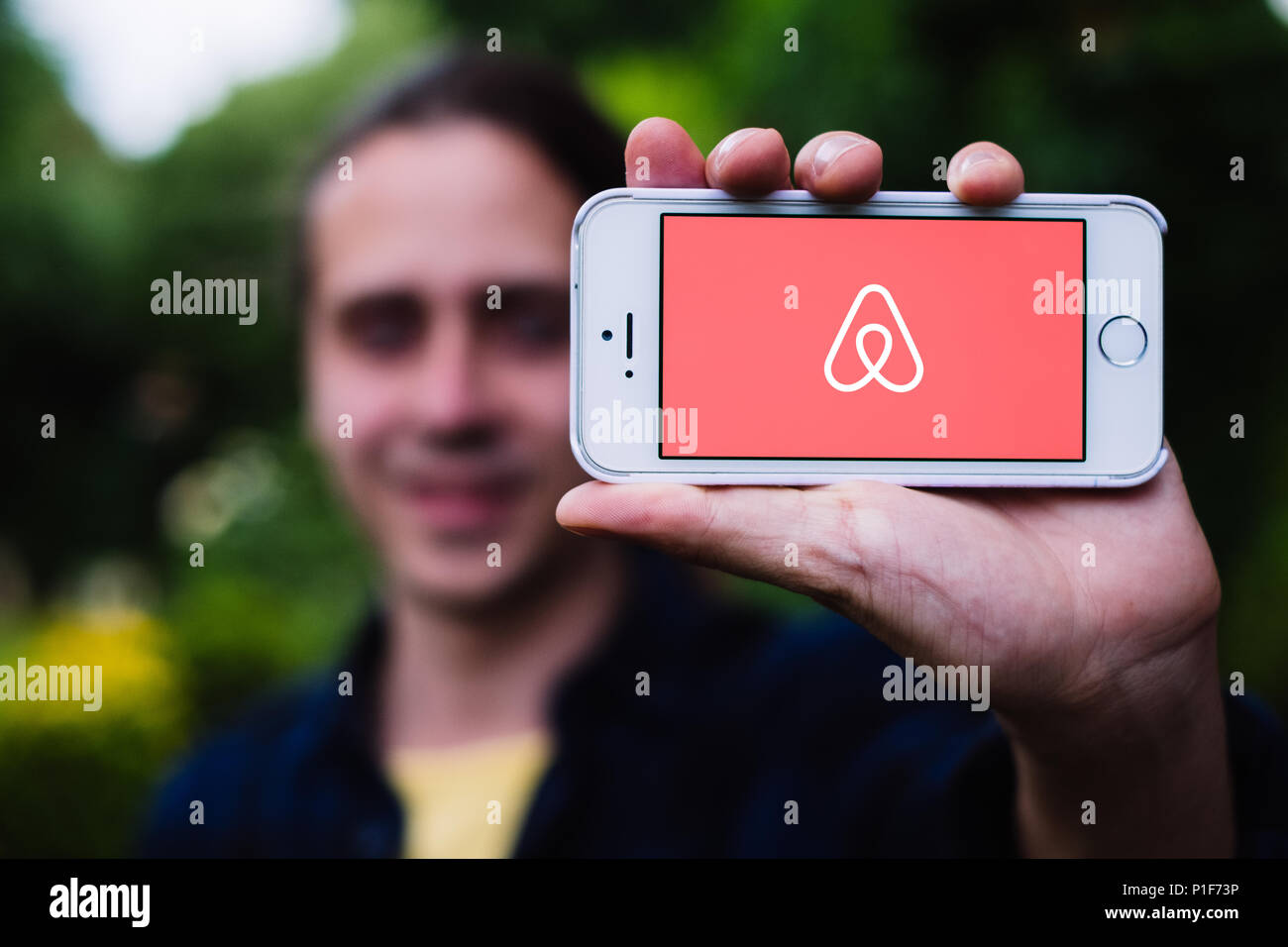 Closeup of young man holding white iPhone with AIRBNB LOGO on screen Stock Photo