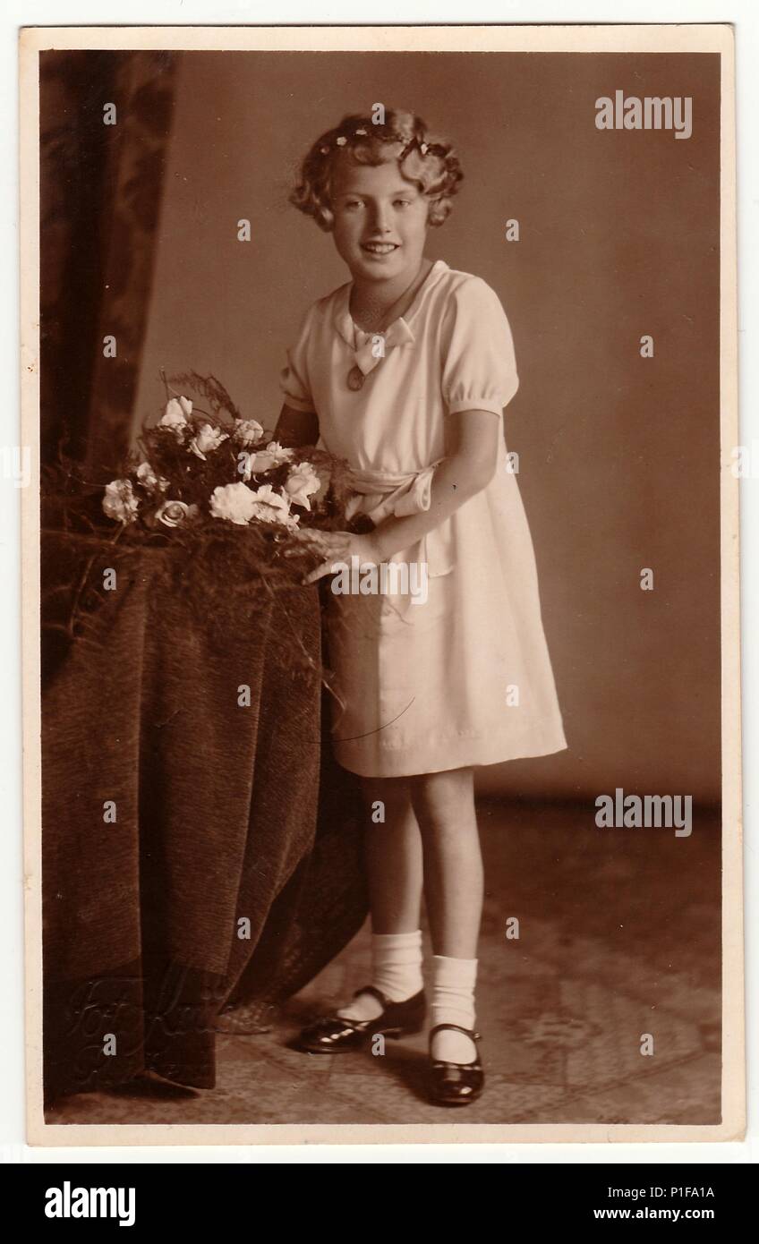 LIBEREC (REICHENBERG), THE CZECHOSLOVAK REPUBLIC - CIRCA 1930s: Vintage photo shows young girl with bouquet poses in a photography studio. Photo with dark sepia tint. Black & white studio portrait. Old photo, 1930s. Stock Photo