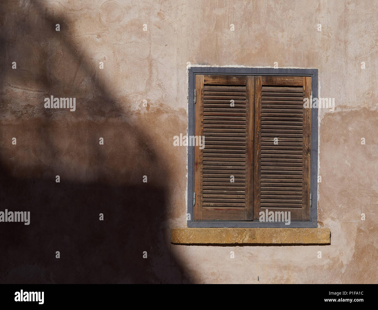 Old city wall with a vintage square window with brown wooden shutters ...