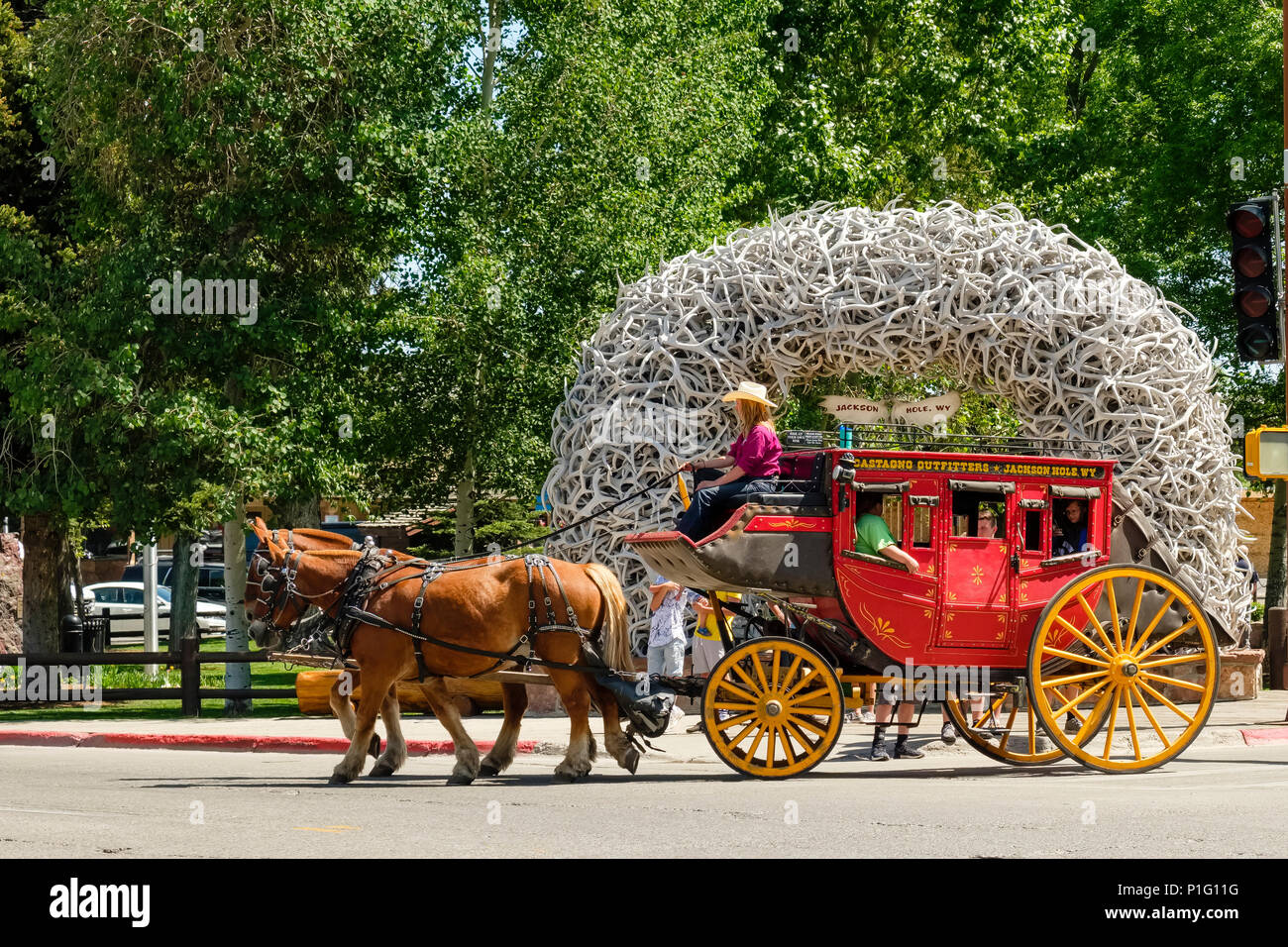 Horse drawn stagecoach typical of old American West carries tourists in Jackson Wyoming in front of iconic park entrance arch of antlers. Stock Photo