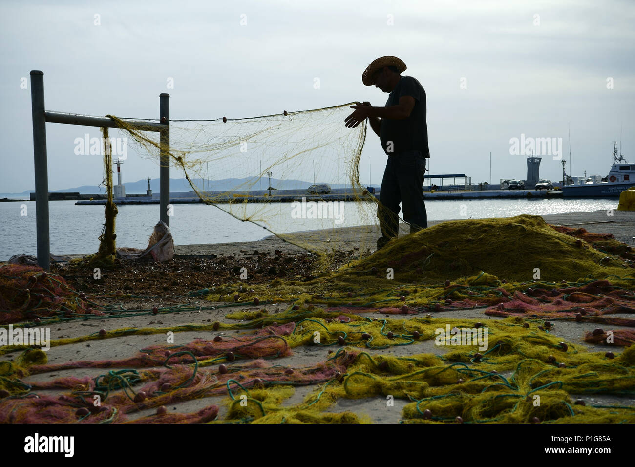 Fisherman cleaning his nets at dock in Tinos, Cyclades islands, Greece Stock Photo