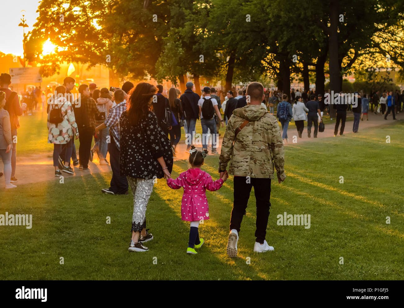 family walking along the park grass on a summer day.Beautiful sunset light. Stock Photo