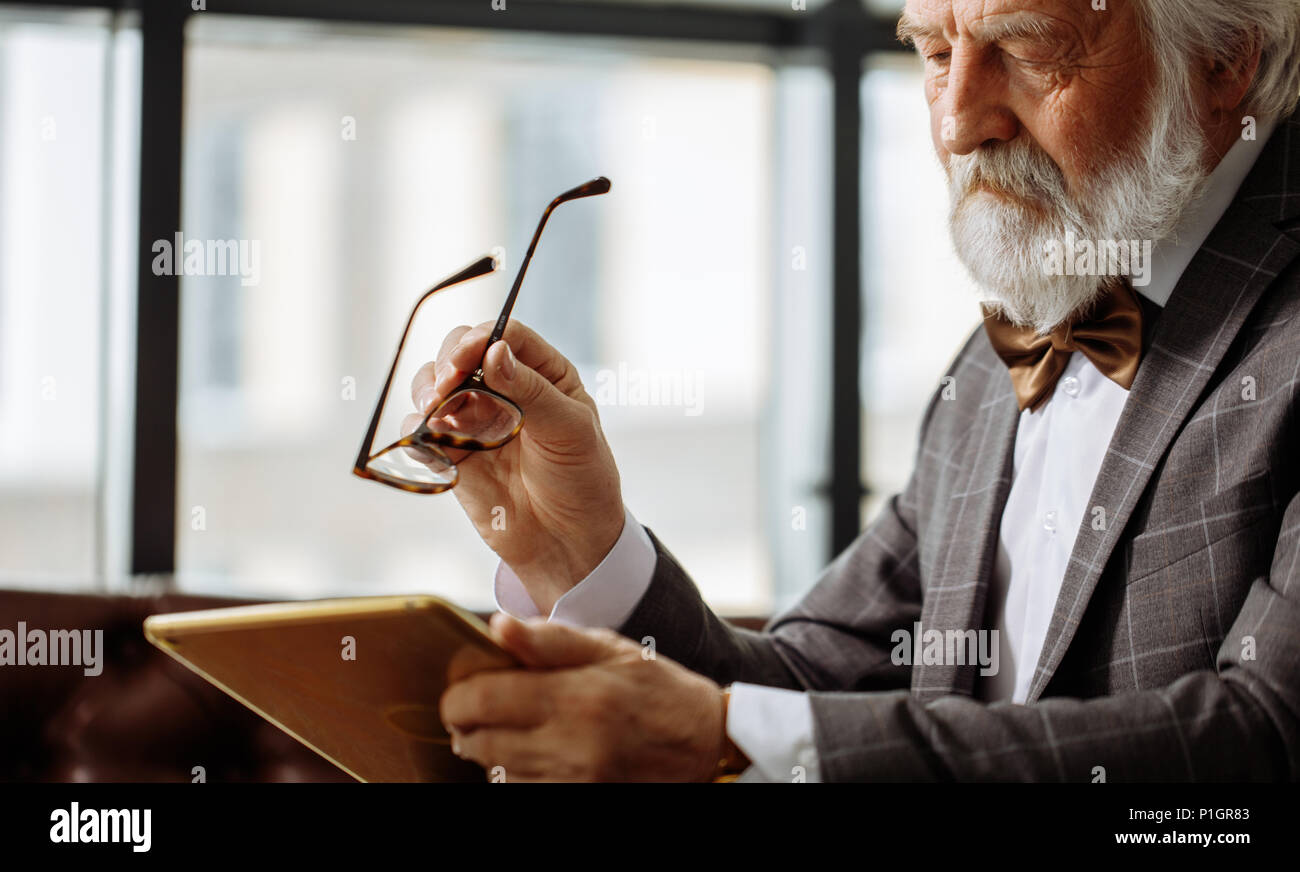 old man with bad eyesight trying to descry an image on the screen of the tablet Stock Photo